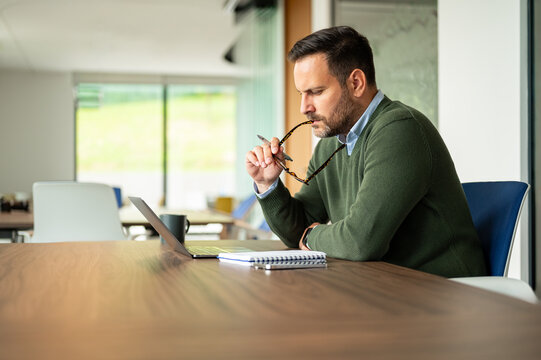 Business executive concentrating on work, biting end of eyeglasses while thinking about a project, analyzing data, and brainstorming new ideas in a modern office