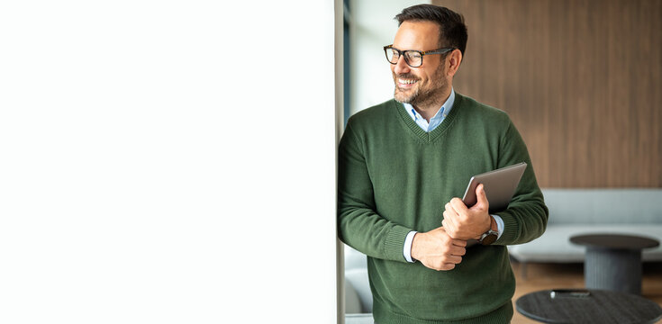 Young entrepreneur embracing digital transformation, confidently holding a tablet while smiling and looking towards new opportunities in a contemporary workspace