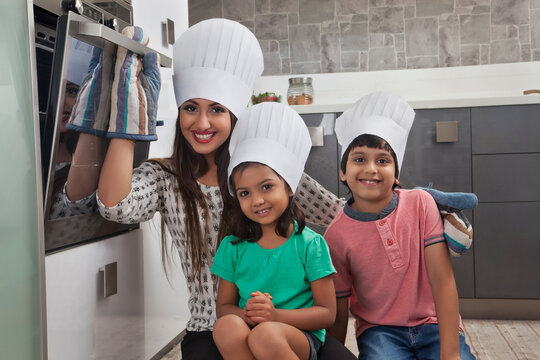 Mother with daughter and son wearing chefs hat and baking cake in kitchen