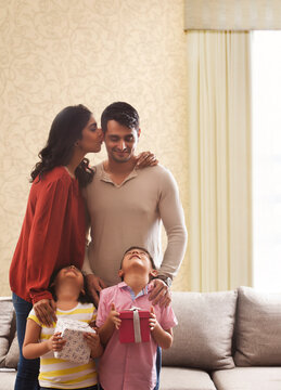 Woman kissing man on cheek,girl and boy holding gifts looking up with heads back 