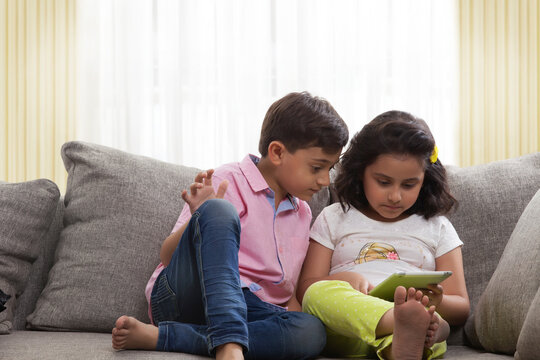Brother and sister sitting on sofa using digital tablet