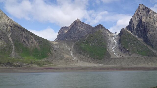 Wide landscape shot revealing the braided river winding through Akshayuk Pass, framed by steep granite cliffs with a receding glacier terminus visible higher up the valley floor.