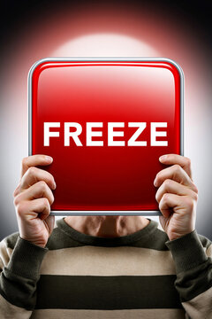 Person h&auml;lt rotes Schild mit Aufschrift Freeze vor dunklem Hintergrund