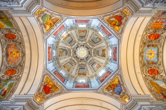 The interior of Basilika St. Lorenz in Kempten. It features a dome with detailed artwork and a bright central light. Visitors admire the architecture and paintings.