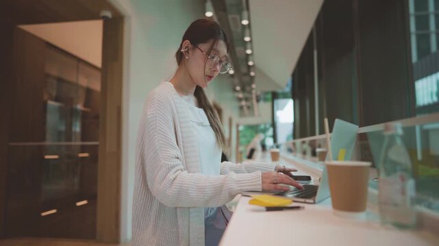 Young adult business asian woman using laptop at co working space wear eyeglasses, wireless headphones urban lifestyles with modern digital technology