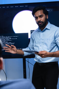 Indian Male Software Project manager Presenting Coding, AI model and Technology Information on big screen to his team while collaboration work, reviewing code, analyzing for development project.
