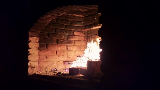 A warm fire burns in a brick fireplace. The flames flicker against the dark background, creating a cozy atmosphere. Logs are visible in the hearth.