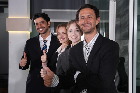 A quiet chuckle escapes the bearded businessman in front as the team holds its final thumbs up pose, four confident happy faces filling the tight close frame completely.