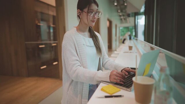 Young adult business asian woman using laptop at co working space wear eyeglasses, wireless headphones urban lifestyles with modern digital technology