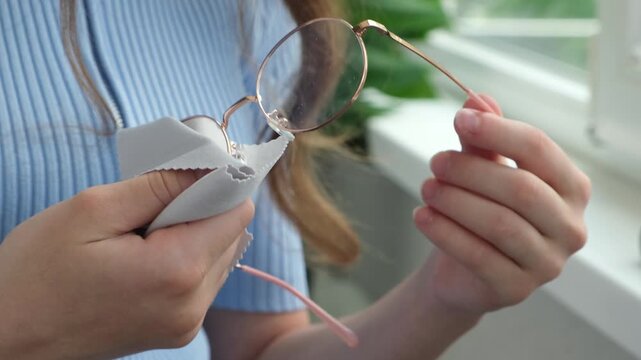 Teen girl's hand wiping glasses lenses with microfiber wipe close up. Person wash eyeglasses with cloth. Concept of good vision and spectacles care