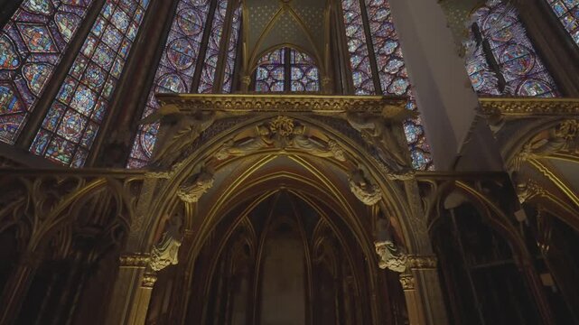 A close view of an ornate gilded altar canopy set against colourful stained glass in a historic Parisian gothic chapel.