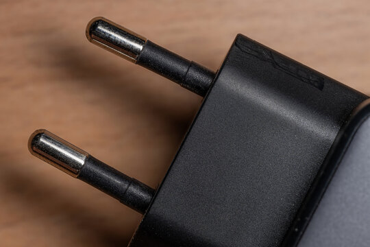 Close-up of a European power adapter plug with two round pins on a wooden background. High-resolution macro photo of an electrical charger with shallow depth of field