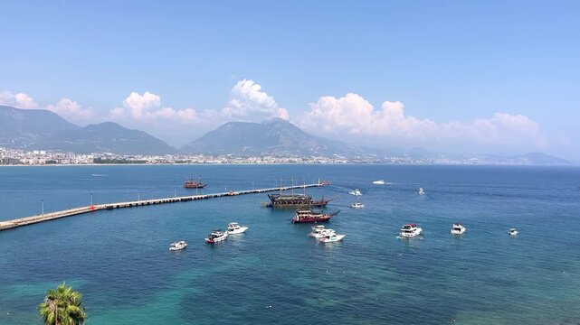 Scenic high angle view of Alanya harbor with tourist pirate ships and yachts floating on turquoise Mediterranean sea water against Taurus mountains in Turkey on a sunny summer day, coastal tourism, se
