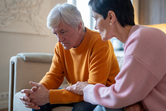 Saddened depressed husband silently sitting on sofa dealing with life problems being comforted by wife, elderly married couple financial and work issues, adversity, understanding, emotional connection