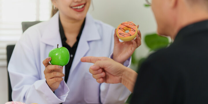 Nutritionist presenting green apple and donut for healthy food choice during patient consultation