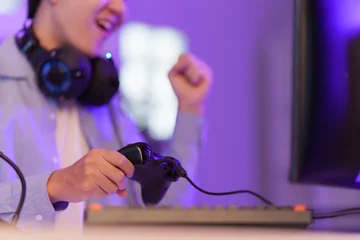 Fotobehang Gaming Asian gamer holding controller celebrating video game victory in purple room  © itchaznong