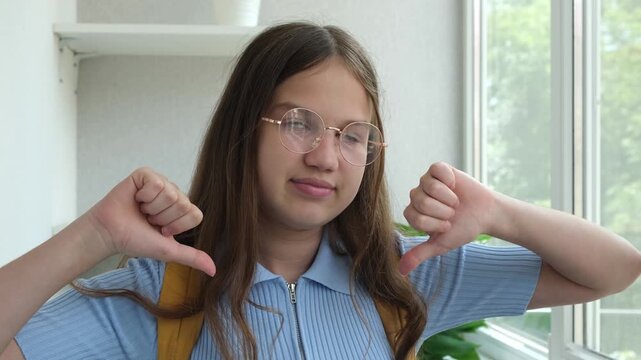 Displeased teen student girl gesturing thumbs down. Female teenager schoolgirl in glasses Judging and disapproving looking at camera. Dislike concept