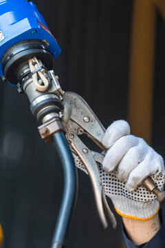 Close-up of industrial robotic welding torch with locking pliers during maintenance in smart factory. Precision engineering, robotic automation, manufacturing technology, equipment repair.