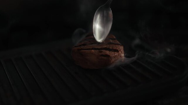 Seared steak on grill with spoon basting in dark moody setting