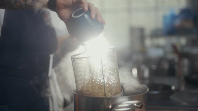 Chef sprinkles seasoning into a pot of steaming food in restaurant kitchen