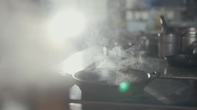 Chef stirs food in a pan with steam rising in a restaurant kitchen