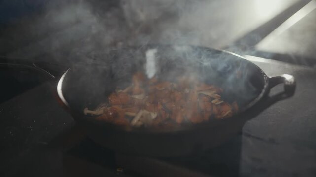 Sizzling food in a dark pan with rising steam and smoke