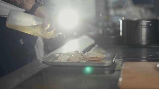 Chef drizzles sauce over scallops on a metal tray in kitchen