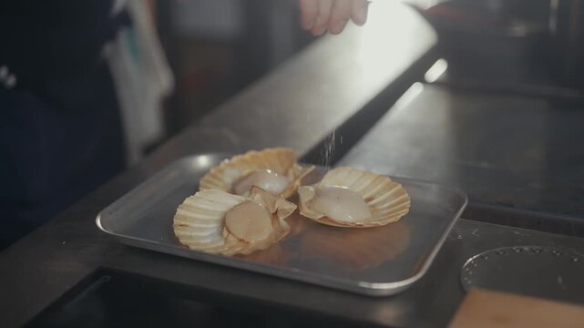 Chef seasons fresh scallops on a metal tray in a restaurant kitchen