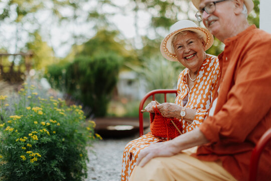 Happy senior couple sitting together in garden bench, smiling and looking at camera.
