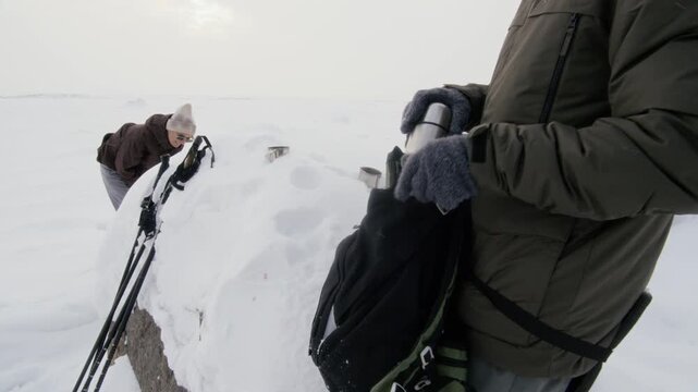 Caucasian adult man packing thermos into backpack and putting it on during winter hike with adult woman. Ideal for outdoor recreation brands and winter adventure campaigns