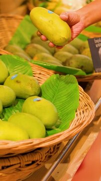 Customer Selecting Fresh Green Mangoes in a Thai Market