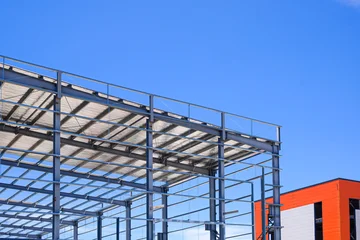 Steel frame structure of modern industrial warehouse under construction with bright blue sky © Prapat