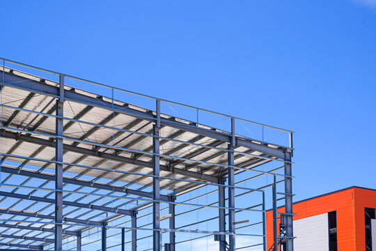 Steel frame structure of modern industrial warehouse under construction with bright blue sky