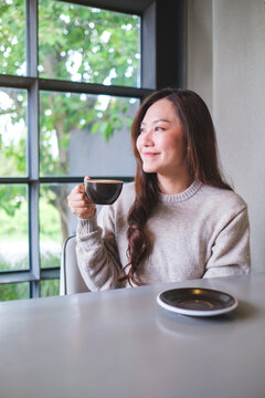 Vertical portrait image of a woman holding and drinking hot coffee in cafe