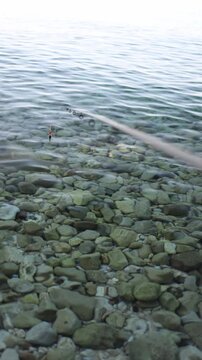 Vertical screen Float fishing on crystal clear water highlights sensitive bite detection above rocky bottom bringing peaceful focus to every gentle movement below surface