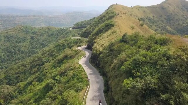 Winding mountain road aerial view, scenic asphalt highway through lush green hills, tropical forest landscape with curved path for travel and road trip
