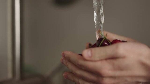 Slow motion closeup shot of man washing cherries with kitchen faucet
