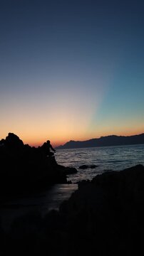 Vertical screen Sunset fishing silhouette on rocky Adriatic coast captures peaceful evening solitude calm sea horizon and mindful travel moments after a warm summer day