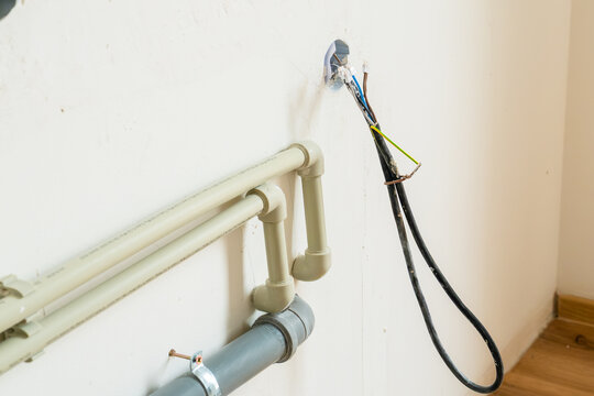 Installing PVC plumbing pipes alongside electrical wiring within a wall cavity during home renovation. The setup includes visible connections for water supply and electrical lines. 