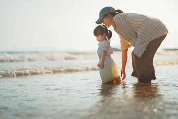 Happy Asian mother and cute little daughter playing in sea water on sandy beach at sunset, family enjoying tropical ocean travel vacation during golden hour, child development, parenting and summer © oatawa