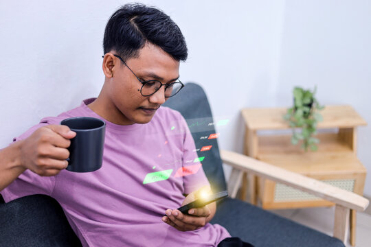 Man Sitting on Couch Holding Mug and Using Smartphone to Track Financial Hologram at Home