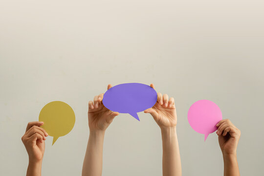 Raised hands hold colorful speech bubbles against a plain background