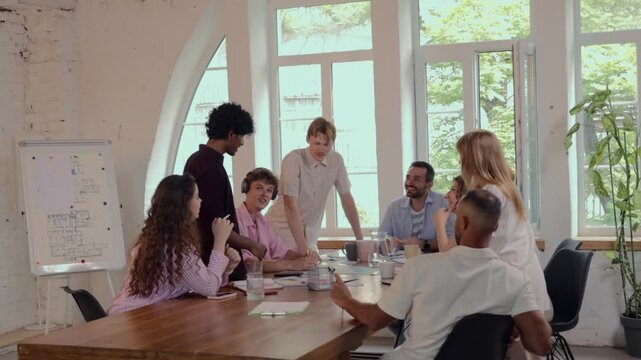 Excited diverse coworkers celebrating team success with high fives during office meeting. Concept of corporate achievement, employee recognition, positive workplace culture.