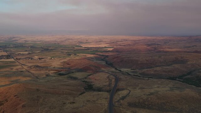 Aerial of winding road through arid rolling hills and valley in Midvale Idaho with thick wildfire smoke at sunset in summer