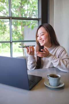 Vertical of a woman holding smart phone and using voice messaging, talking with ai assistant for Artificial intelligence concept while working on laptop