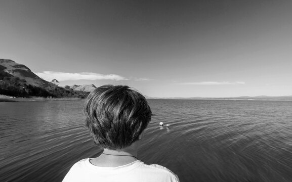 black and white image of teenage boy looking out at Grotto Lagoon from pier, Hermanus, South Africa