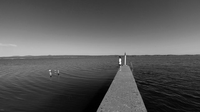 black and white image of teenage boy looking out at Grotto Lagoon from pier, Hermanus, South Africa
