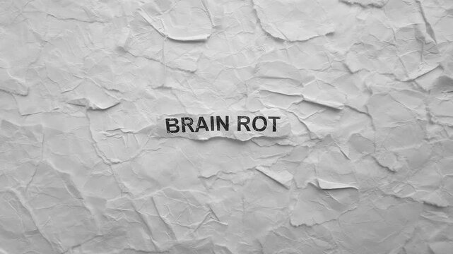 Crumpled piece of paper with words Brain Rot on torn crumpled white paper pieces background