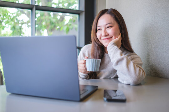 Portrait image of a woman drinking coffee while working on laptop computer