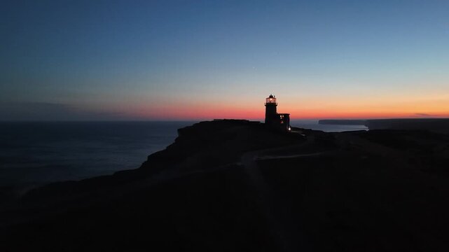 Beacon shining at St Aldhelm Head lighthouse on the coast of England during sunrise
